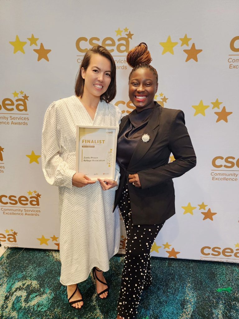 A picture of two female staff against a white promotional CSEA background with gold stars holding a white A4 frame with the finalist certificate.